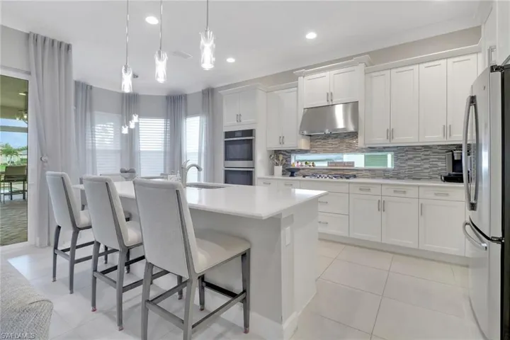 Kitchen with sink, a kitchen island with sink, white cabinetry, stainless steel appliances, and decorative light fixtures