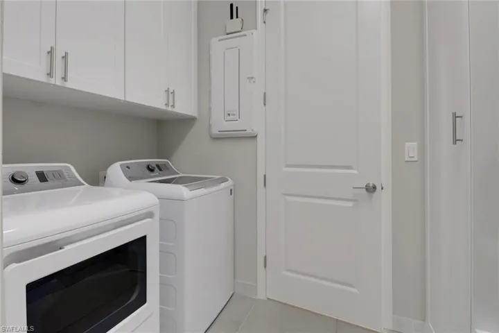 Clothes washing area with cabinets, separate washer and dryer, light tile patterned floors, and electric panel