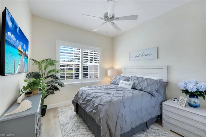 Bedroom featuring wood-finish flooring, vaulted ceilings, a ceiling fan, and plantation shutters onlooking the pool with a lake view.