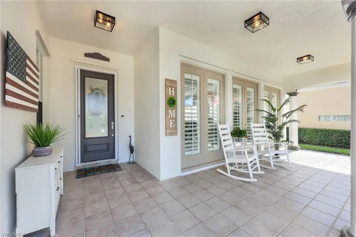 Covered porch with square tile flooring, entry door with decorative glass, and French doors featuring interior plantation shutters.