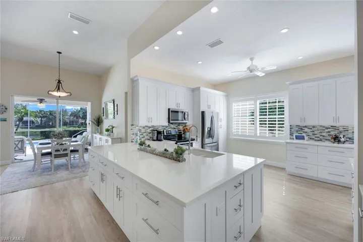 Expansive remodeled kitchen featuring an expansive central island with an integrated sink, white shaker-style cabinetry, stainless steel appliances, and wood-finish flooring.