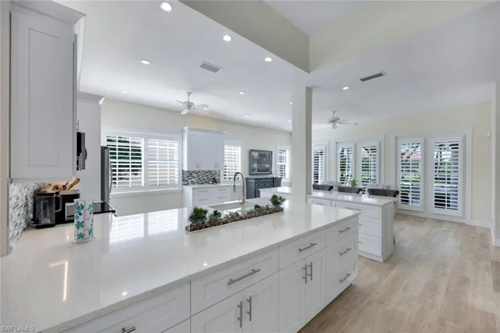 Expansive fully remodeled kitchen featuring a large island with a light-colored countertop, white shaker-style cabinetry with chrome hardware, and a mosaic tile backsplash