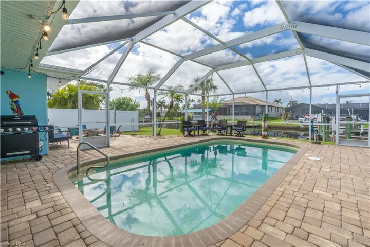 Outdoor pool featuring glass enclosure, a patio, a sunroom, and a grill