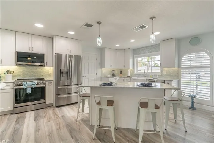 Kitchen featuring appliances with stainless steel finishes, hanging light fixtures, light wood-type flooring, white cabinets, and recessed lighting