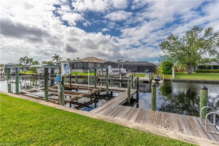 Dock featuring a lawn, a water view, boat lift, and a residential view