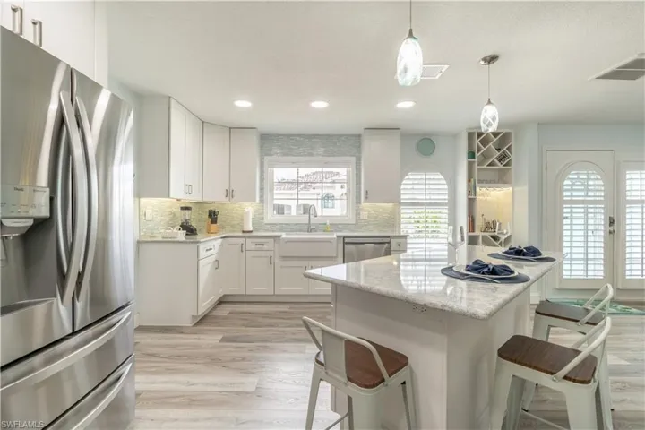 Kitchen with appliances with stainless steel finishes, white cabinets, light stone counters, light wood finished floors, and a breakfast bar