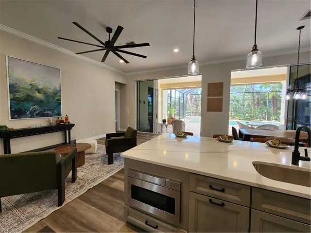 Kitchen with light stone counters, dark wood-type flooring, decorative light fixtures, ornamental molding, and a ceiling fan