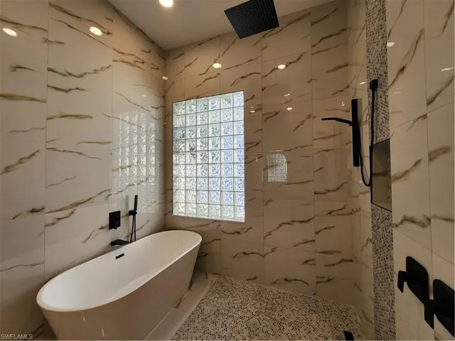 Full bath featuring tile walls, a freestanding tub, a marble finish shower, and recessed lighting