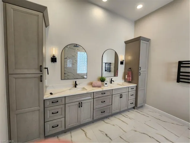 Bathroom with double vanity, light marble finish flooring, and recessed lighting