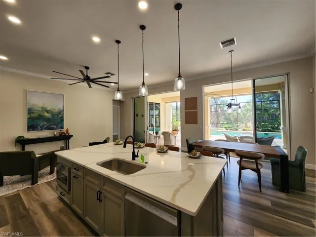Kitchen featuring light stone counters, dark wood finished floors, dishwashing machine, an island with sink, and ornamental molding