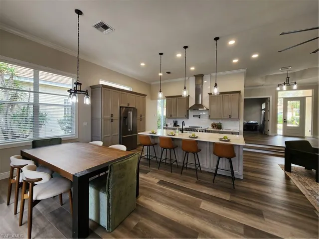 Kitchen with a breakfast bar, a large island with sink, stainless steel refrigerator, range hood, and ornamental molding