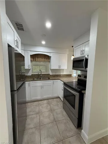Kitchen with a sink, visible vents, white cabinetry, fridge, and range