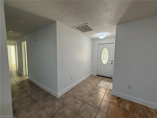 Entryway with tile patterned flooring, visible vents, a textured ceiling, and baseboards