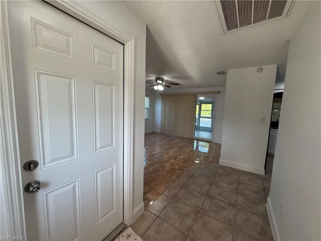 Hall with tile patterned flooring, visible vents, a textured ceiling, and baseboards