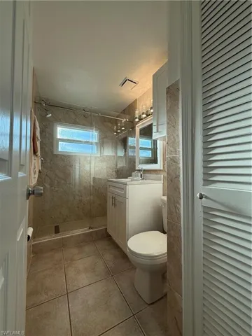 Full bathroom featuring a stall shower, toilet, tile patterned floors, vanity, and tile walls