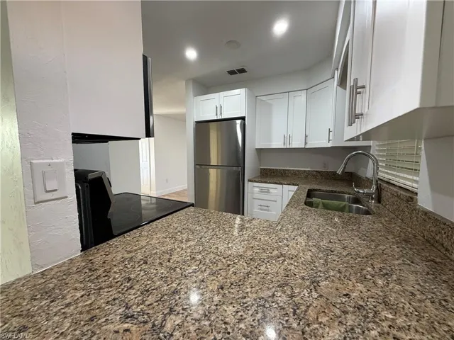 Kitchen with stove, a sink, white cabinets, freestanding refrigerator, and dark stone countertops