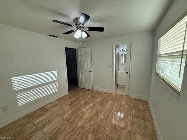 Unfurnished bedroom with a ceiling fan, connected bathroom, visible vents, and baseboards