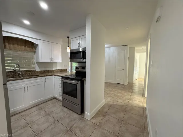 Kitchen with white cabinets, light tile patterned floors, stainless steel appliances, and a sink