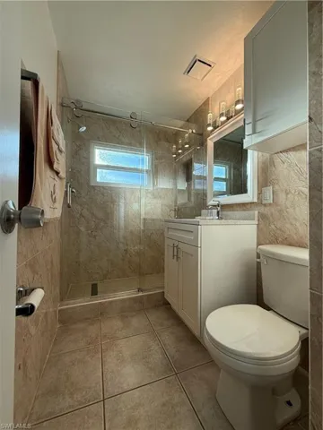 Bathroom with toilet, vanity, tile walls, a shower stall, and tile patterned floors