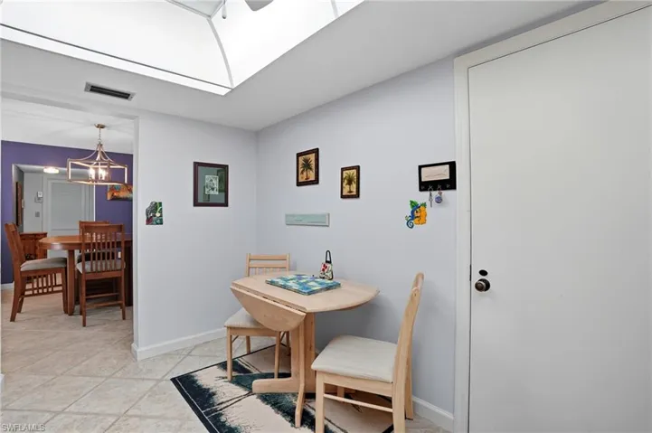 Recessed ceiling with an overhead skylight, tile flooring, and a dining area with a contemporary chandelier