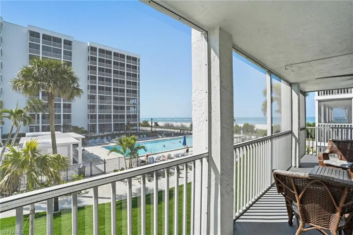 Screened balcony overlooking a pool, manicured lawn, and beach