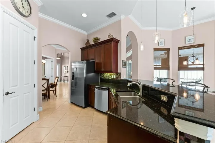Kitchen featuring granite countertops, arched walkways, decorative light fixtures, light tile patterned floors, and ornamental molding