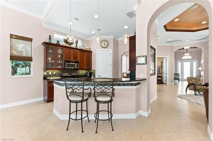 Kitchen featuring a breakfast bar, healthy amount of natural light, decorative backsplash, glass fronted cabinets, and ornamental molding