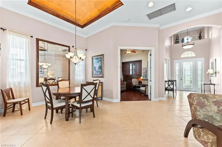 Dining space with healthy amount of natural light, a chandelier, crown molding, light tile patterned floors, and ceiling fan