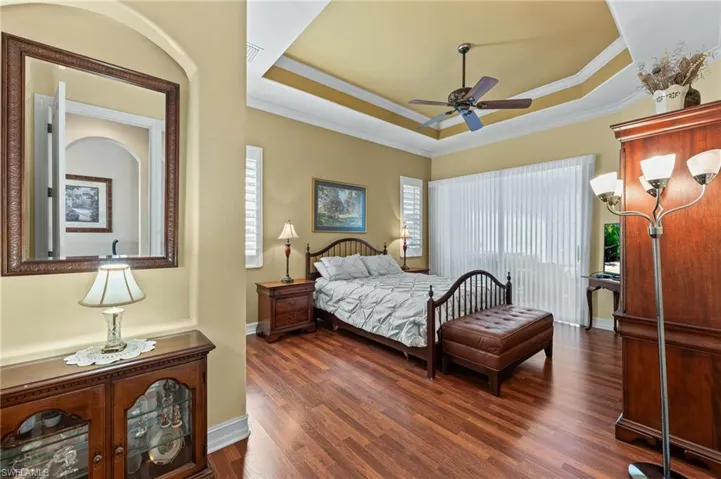 Bedroom with wood flooring, a tray ceiling, ornamental molding, and ceiling fan