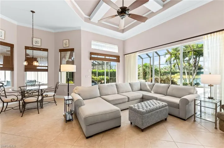 Living room featuring a high ceiling, light tile patterned flooring, ornamental molding, ceiling fan, and suspended lighting