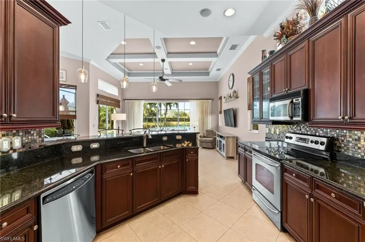 Kitchen featuring backsplash, stainless steel appliances, coffered ceiling, granite counters, and pendant lighting