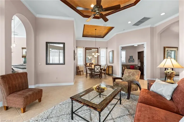 Living area featuring arched walkways, a ceiling fan, ornamental molding, tile patterned floors, and a tray ceiling