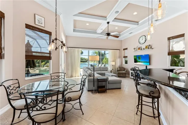 Dining room with coffered ceiling, a ceiling fan, light tile patterned floors, crown molding, and a chandelier
