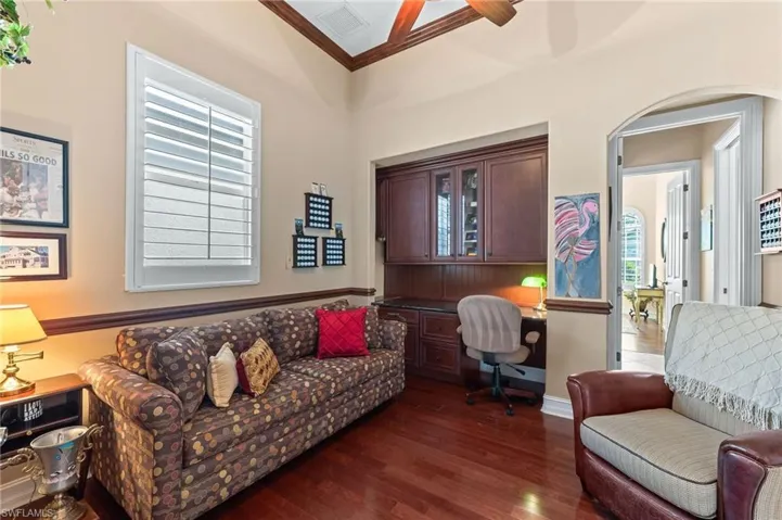 Home office with built in desk, wood floors, ornamental molding, arched walkways, and a ceiling fan
