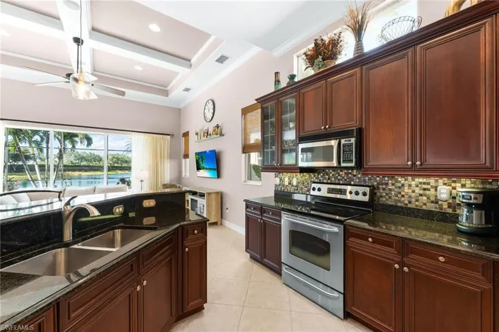 Kitchen with stainless steel appliances, granite counters, coffered ceiling, glass fronted cabinets, and a ceiling fan