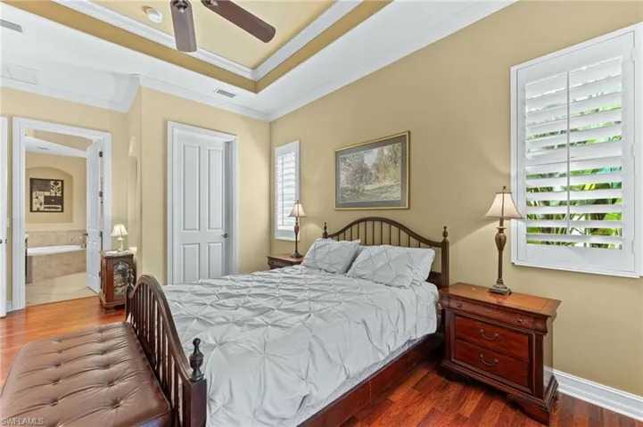 Bedroom with wood floors, a ceiling fan, crown molding, ensuite bath, and a tray ceiling