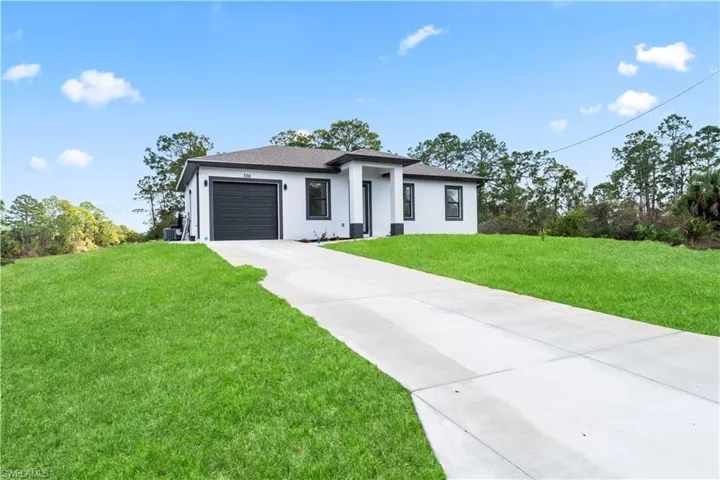 Prairie-style house with a front lawn, driveway, an attached garage, stucco siding, and roof with shingles