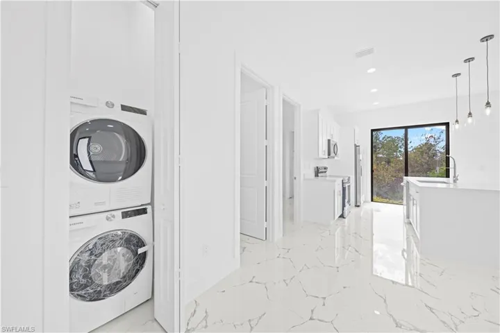 Laundry area featuring stacked washer and clothes dryer, recessed lighting, and light marble finish floors