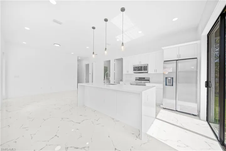 Kitchen featuring stainless steel appliances, white cabinetry, light stone countertops, a center island with sink, and decorative light fixtures