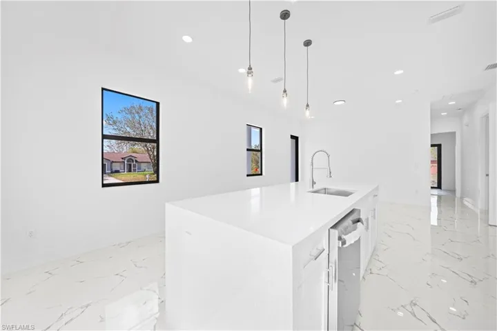 Kitchen featuring light stone countertops, an island with sink, white cabinetry, decorative light fixtures, and light marble finish flooring