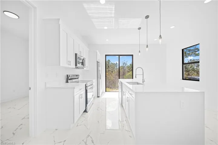 Kitchen featuring a kitchen island with sink, stainless steel appliances, white cabinetry, and light marble finish flooring