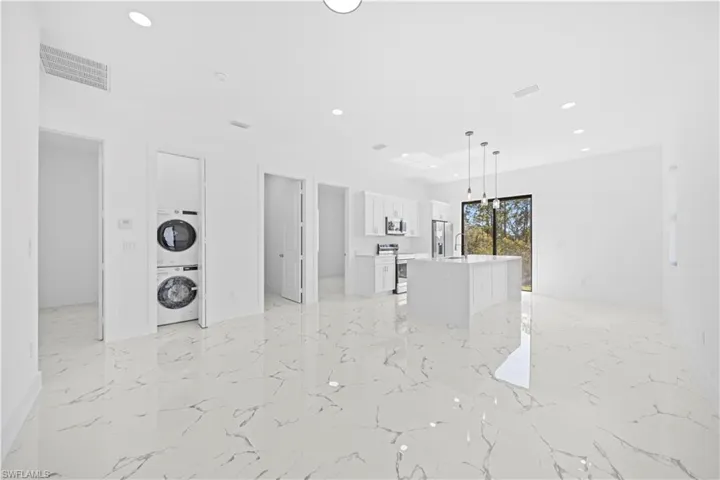 Kitchen with open floor plan, white cabinets, a center island with sink, hanging light fixtures, and stainless steel appliances