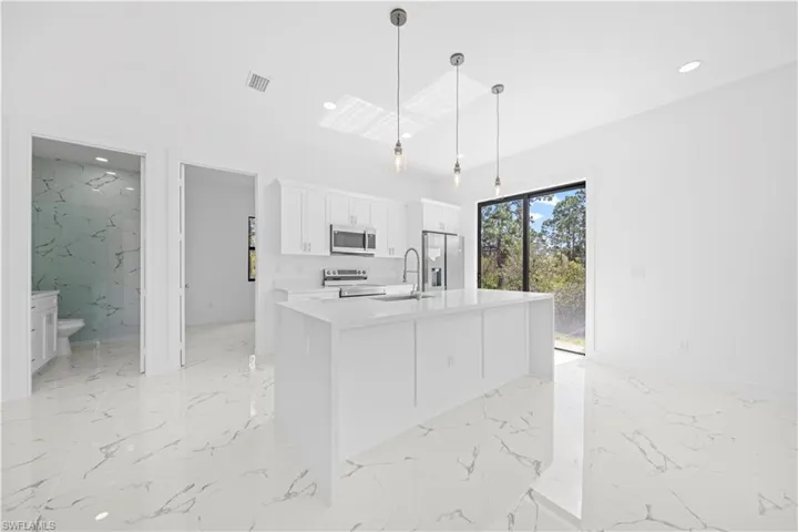 Kitchen featuring stainless steel appliances, light stone counters, pendant lighting, white cabinets, and an island with sink