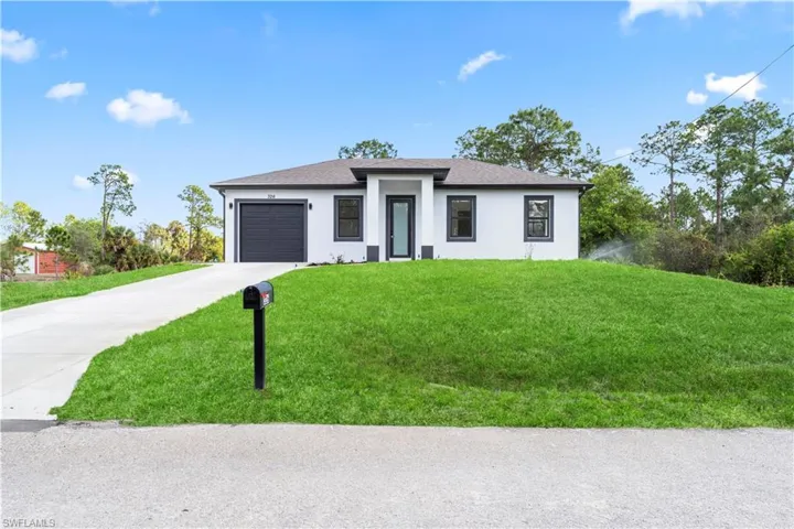 Prairie-style home with stucco siding, a front lawn, driveway, an attached garage, and a shingled roof