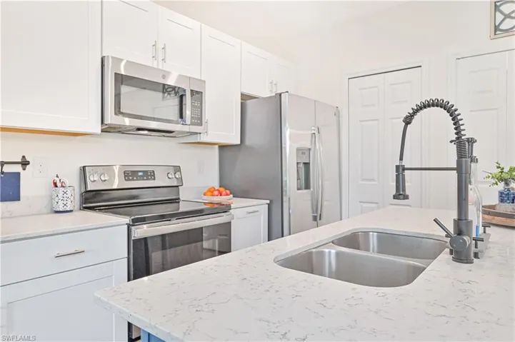 Kitchen with light stone counters, white cabinetry, sink, and stainless steel appliances