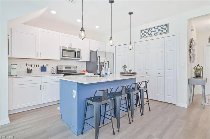 Kitchen with stainless steel appliances, light hardwood / wood-style floors, white cabinets, and a kitchen island with sink