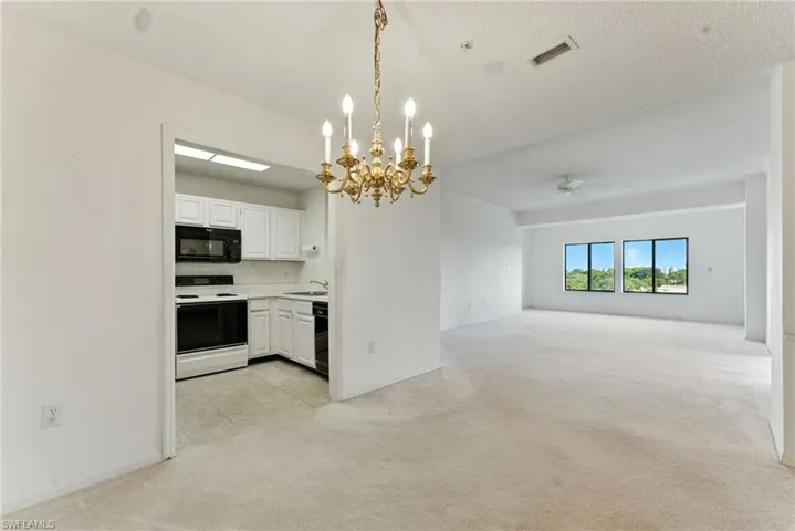 Kitchen with a chandelier, light carpet, light countertops, white cabinetry, and decorative light fixtures