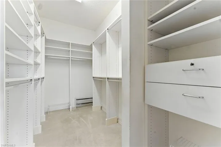 Spacious closet with light colored carpet and a baseboard radiator