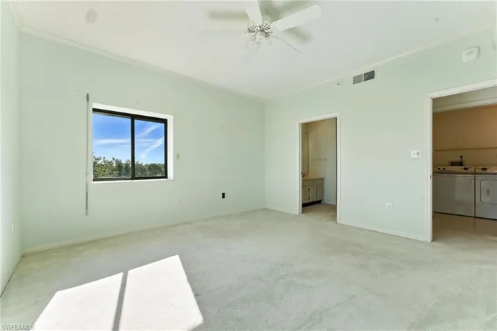 Unfurnished bedroom with light colored carpet, ornamental molding, a ceiling fan, washing machine and clothes dryer, and ensuite bath