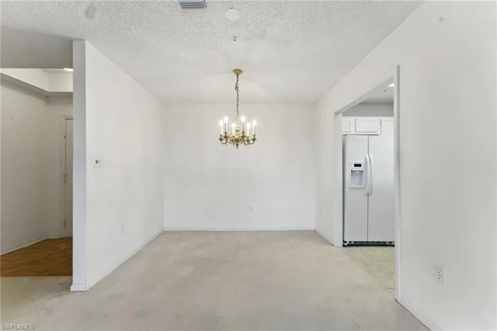 Unfurnished dining area featuring light carpet, a chandelier, and a textured ceiling